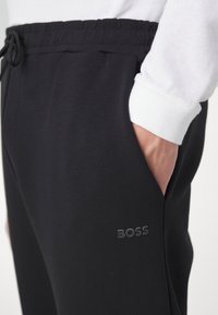 Mustad puuvillased dressipüksid elastse vöökohtadega, külgtaskute ja õrnalt reljeefse "BOSS" logo kaunistusega reie peal.