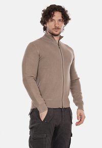 Maglione beige a coste con zip, collo alto, maniche lunghe e design aderente, abbinato a pantaloni cargo scuri.