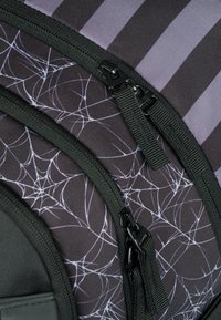Zaino nero con motivo a ragnatela e strisce viola. Presenta numerosi zip e un tessuto testurizzato, con accessori in hardware resistente.