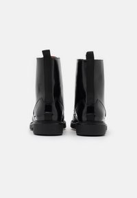 Zwarte gepatenteerde leren enkelboots met elastische zijpanelen en een platte rubberen zool, voorzien van een slanke, glanzende afwerking.