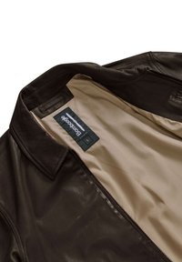 Interno di una giacca di pelle marrone scuro con rivestimento beige; presenta un'etichetta con il nome del marchio e la taglia, e un design del colletto classico.