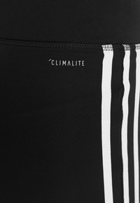 Leggings atléticos negros con rayas verticales blancas, una textura suave y un logo "CLIMALITE" cerca de la cintura.