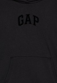 Juodas kapučino džemperis su priekinėmis kišenėmis ir siuvinėtu "GAP" logotipu tos pačios juodos spalvos, pagamintas iš minkštos medvilnės mišinio medžiagos.