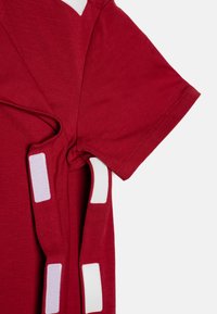 Rød kortærmet t-shirt lavet af blød bomuld, med hvide og lyserøde pletter på siderne og skulderne, i en afslappet pasform.