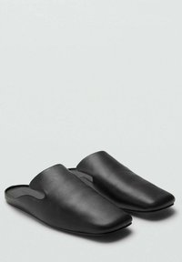 Mule nere in pelle con punta affusolata, caratterizzate da ritagli laterali e una superficie liscia. La suola è piatta e minimalista.