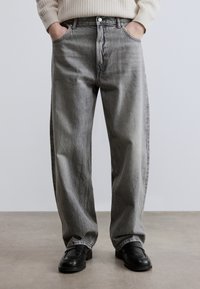 Γκρι τζιν denim με άνετη γραμμή, πέντε τσέπες και κούμπωμα με κουμπί. Διαθέτει ξεθωριασμένη υφή και ίσιο σχέδιο ποδιού. Φοράει μαύρα loafers.