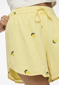Svetle žluté kraťasy s elastickým pasem a stahovací šňůrkou, s vyšitými vzory citronů a měkkou, texturovanou tkaninou.