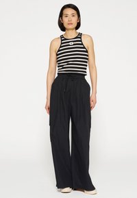 Zwart-wit gestreepte tanktop met ronde hals, gecombineerd met loszittende zwarte broek met een elastische tailleband en zakken.