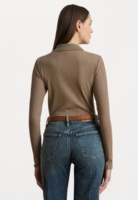 Top castanho com ribas de mangas compridas combinado com jeans de denim azul de cintura alta e um cinto de couro castanho, exibindo uma silhueta ajustada.