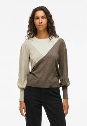 Brun og beige strikket sweater med et trekantet farveblokdesign, lange puffærmer og en tætsiddende kant. Sammen med sorte bukser.