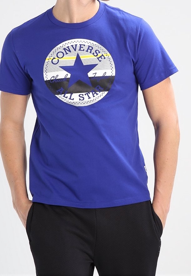 T-shirt en coton bleu avec un grand motif d'étoile noire et le texte "Converse All Star" en design circulaire. Manches courtes et col rond.