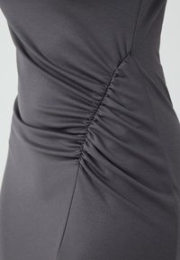 Abito grigio aderente realizzato in tessuto morbido, con dettagli arricciati su un lato e una trama liscia. Progettato per una silhouette contornata.
