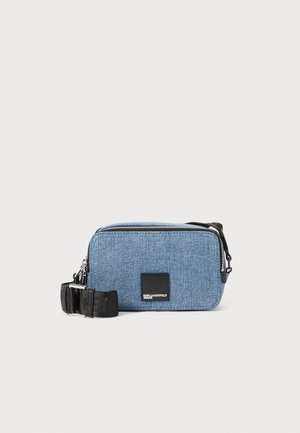 Denim pouch bag in light blue with a black zipper, black strap, and logo patch on the front. Rectangular shape with a smooth texture.
