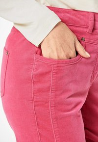 Aangepaste roze corduroy broek met zijzakken, zichtbare stiksel-details en glanzende metalen knoopaccenten in de taille.