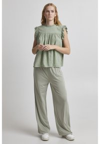 Light green top with ruffled shoulders and embroidered details, paired with loose-fitting light green pants and white sneakers.