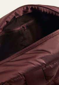 Burgundy hátizsák belseje sima anyagból készült, hálós cipzáras zsebével és párnázott szélekkel rendelkezik. Cipzáras záródással és állítható pántokkal rendelkezik.