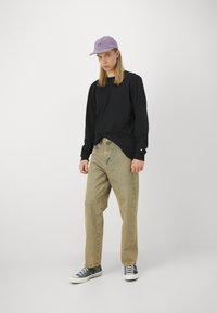 Black long-sleeve shirt, light beige denim pants, lavender cap, and navy sneakers with white soles. Simple, relaxed fit, minimal detailing.