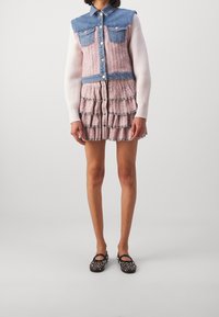 Robe en denim et tissu texturé avec un corsage ajusté, une jupe à volants superposés et une fermeture à boutons. Des chaussures noires cloutées complètent la tenue.