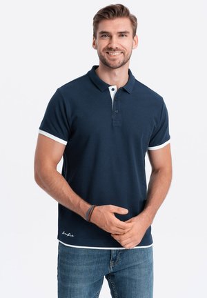 Camiseta polo en color navy con cuello y acentos de manga en blanco, confeccionada en una mezcla de algodón, que cuenta con una tapeta de tres botones y un logo bordado en el dobladillo.