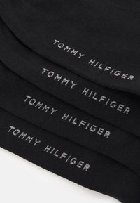 Crne čarape s natpisom "TOMMY HILFIGER" u sivoj boji. Imaju mekanu teksturu s glatkim, pletenim završetkom.