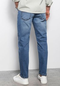 Jeans de mezclilla azul claro con un corte recto, que cuentan con un diseño clásico de cinco bolsillos y puños enrollados, combinados con zapatillas blancas.