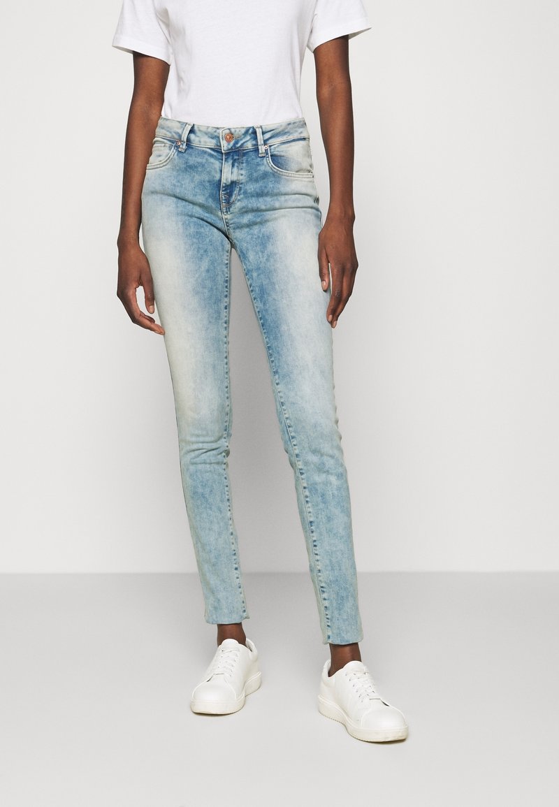 Jeans de denim azul claro con un acabado desgastado, diseño de alta cintura, estilo de cinco bolsillos y un corte ajustado, combinados con zapatillas blancas.