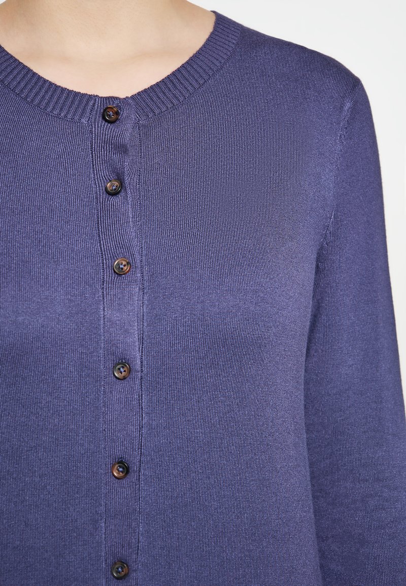 Donkerpaarse cardigan met een ronde halslijn, ribbelranden en zes bruine knopen aan de voorkant, gemaakt van een textuur gebreide stof.