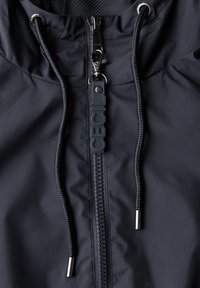 Černá zipová bunda s texturovanou tkaninou, která má výrazný zip a logo na táhle, a nastavitelné tkaničky na kapuci.