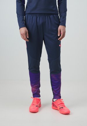 Laivaston urheiluhousut, joiden alaosassa on violetti kuvio ja joustava vyötärönauha, yhdistettynä kirkkaan pinkkeihin jalkapallokenkiin, joissa on mustia yksityiskohtia.