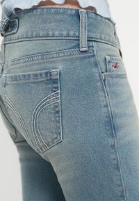 Ανοιχτό μπλε τζιν παντελόνι με πίσω τσέπες που έχουν διακοσμητικές ραφές και μια μικρή ετικέτα με λογότυπο. Το ύφασμα έχει ομαλή υφή.