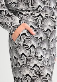 Mustekku ja valkoinen kuvioitu kangas, jossa fanikuvioita, näkyvissä oleva tasku sivussa, sileä tekstuuri ja pehmeä laskeutuminen.