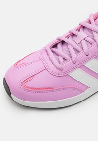 Sportovní obuv v růžovém syntetickém materiálu s bílými pruhy. Má texturovaný povrch, zaoblený tvar a kontrastní růžové akcenty.