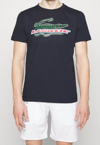 Navyblå bomullströja med en grön krokodil-logotyp och färgglada bokstäver. Standardpassform med korta ärmar och rundad halsringning.