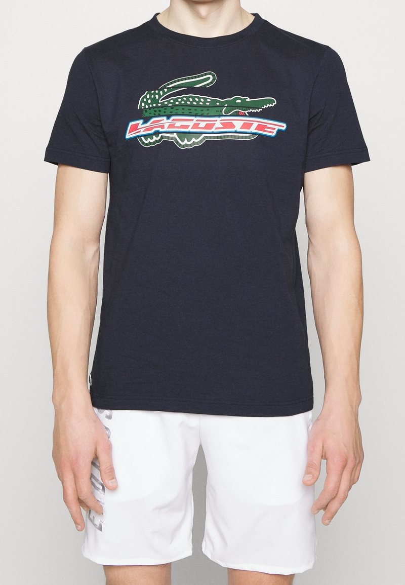 Navyblå bomullströja med en grön krokodil-logotyp och färgglada bokstäver. Standardpassform med korta ärmar och rundad halsringning.