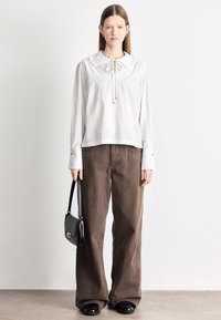 Biała i kremowa bluzka w paski z falbankowym kołnierzem i wiązaniem, zestawiona z szerokimi brązowymi spodniami i czarną torebką. Czarne buty z zaokrąglonymi noskami.