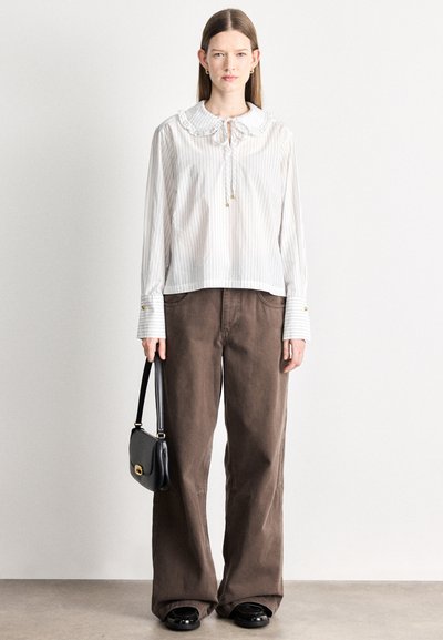 Blouse rayée blanche et crème avec col à volants et détail noué, associée à un pantalon large marron et un sac à main noir. Chaussures noires à bouts arrondis.