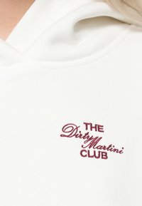 Λευκή hoodie με μαλακή υφή και μπροστινή τσέπη. Κεντημένος χαρακτήρας σε βουργουνδί αναγράφει "THE Dirty Martini CLUB" κοντά στη λαιμόκοψη.