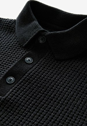 Sort polo-shirt i struktureret strikstof, med en klassisk krave og tre sorte knaplukninger foran.