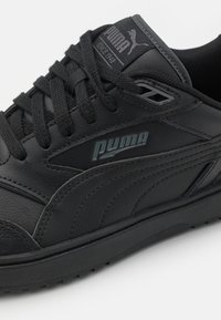 Černé kožené tenisky s texturovaným povrchem, s tlustou podrážkou, černými tkaničkami a jemným embosovaným logem Puma na boku.