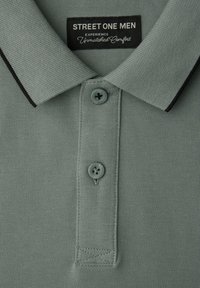 Polo pour homme gris clair avec col bordé de noir, deux boutons et étiquette "STREET ONE MEN" au niveau du col.