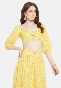 Completo a due pezzi giallo a quadri, composto da un top corto con maniche a palloncino e dettaglio cut-out, abbinato a una lunga gonna plissettata.