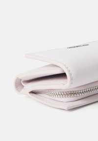 Käytännöllinen vaaleanpunainen lompakko, joka on valmistettu sileästä nahasta. Lompakossa on vetoketjukiinnitys ja huomaamatonta ommeltua yksityiskohtaa reunoilla.