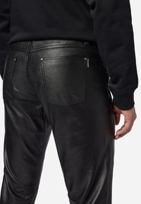 Schwarze Lederhose mit glatter Textur, die zwei Gesäßtaschen und Nahtakzente aufweist. Der Bund hat ein Etikett auf der Rückseite.