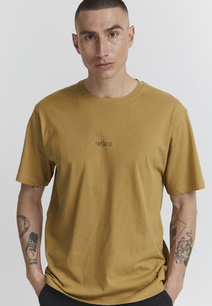 Mosterdkleurig katoenen T-shirt met een ronde hals en korte mouwen, voorzien van een klein bedrukt tekstontwerp aan de voorkant.