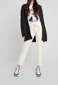 Černý pletený cardigan, bílé tričko s grafikou, krémové rovné džíny a tenisky s akcenty v barvě teal a růžovou podrážkou. Neformální outfit.