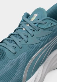 Μπλε αθλητικό παπούτσι με πλέγμα στην επιφάνεια, επενδυμένο περιμετρικά, μπλε κορδόνια και ασημένια ρίγα σε λευκή σόλα, σε κοντινή λήψη.