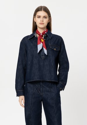 Dark denim jacket with a boxy silhouette, snap buttons, and a chest pocket. Paired with dark denim pants and a red scarf tied at the neck.