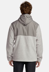 Gray and light gray hooded jacket, featuring a smooth upper section, textured lower section, and elastic cuffs. Back view shown.