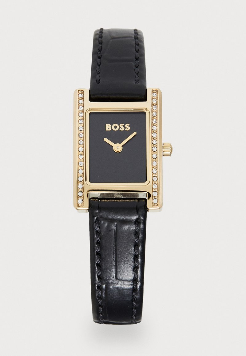 Orologio rettangolare dorato con quadrante nero. Il cinturino in pelle nera presenta una texture a pelle di coccodrillo. Accentuato da pietre attorno alla lunetta.