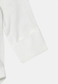 Långärmad vit klädesplaggmanschett med slät textur, synlig sömnad och rak skärning; tyget verkar mjukt och lätt.